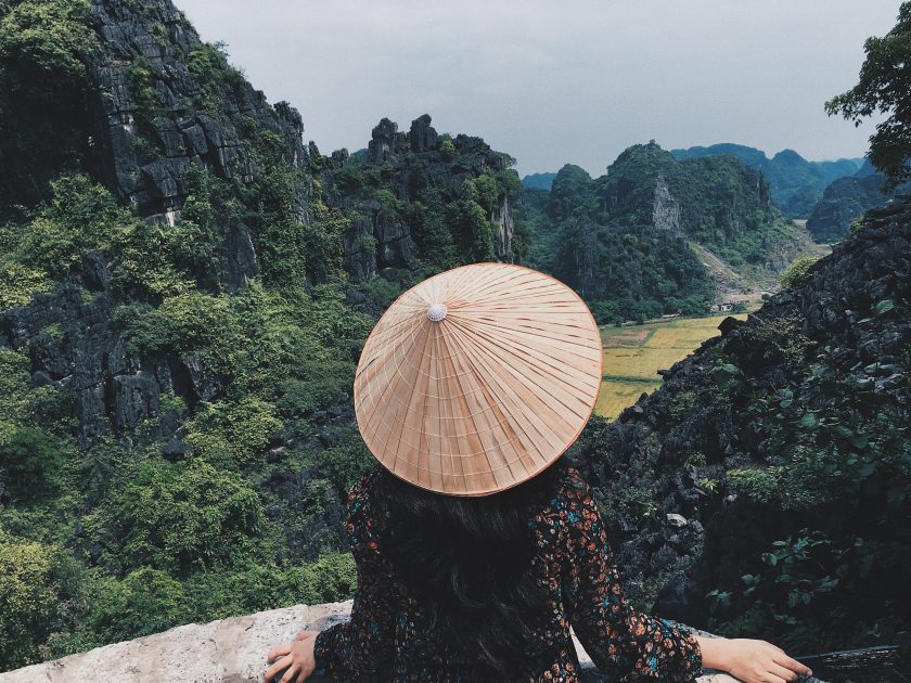 a woman in a traditional conical hat looking out over the mountains