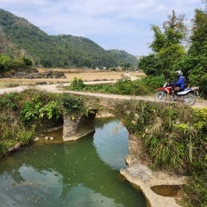 motorcyclist crossing a river on a small bridge in Cao Bang