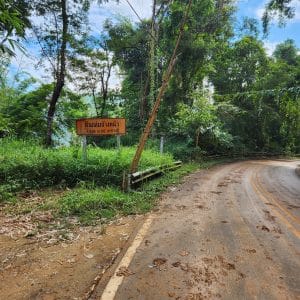 muddy road in northern thailand with a sign warning of landslides.