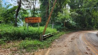 muddy road in northern thailand with a sign warning of landslides.
