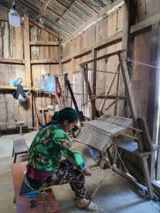 a local woman weaving hemp fabric to make clothing in her stilt house in ha giang