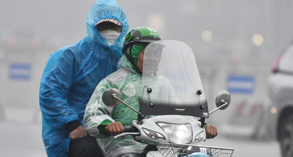 Motorbike taxi rider takes a customer in the misty rain of february in hanoi