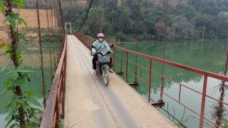 a woman driving over a suspension bridge on a Honda in Ha Giang